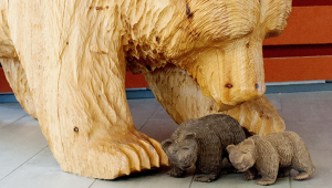 En stor björnskulptur av trä, som föreställer en björn som böjer sig fram över två små björnar i trä framför den.